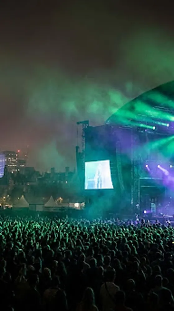 Festival main stage washed in purple and green light through the rain