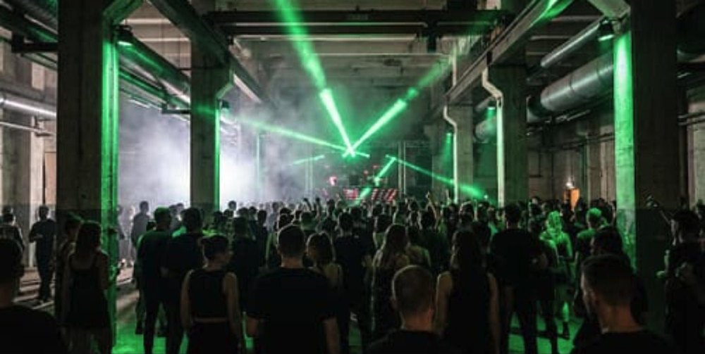 Berlin show: crowd in a concrete warehouse under green beams